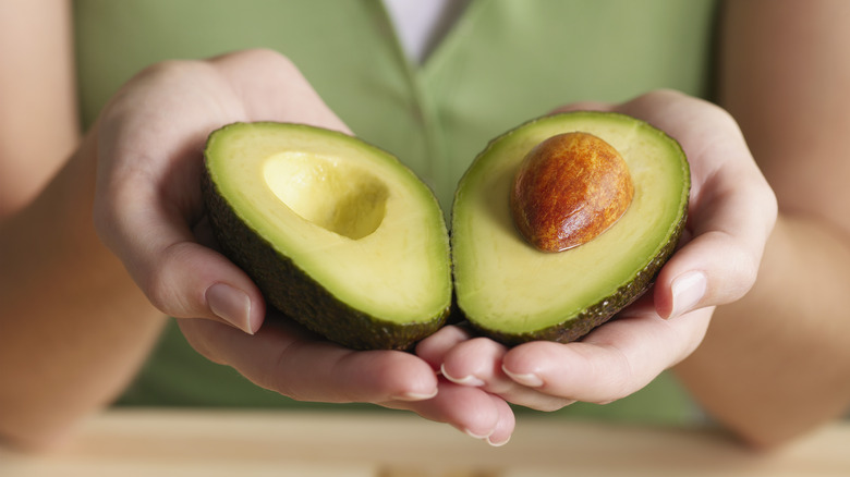 Two hands holding a sliced avocado