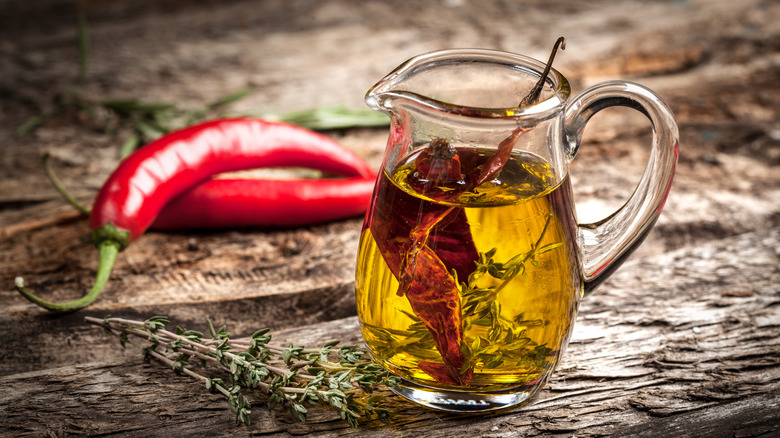 Olive oil in a glass with fresh herbs and spicy peppers infusing it