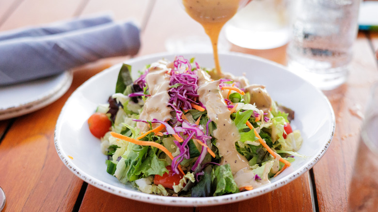 Someone adds dressing to a salad
