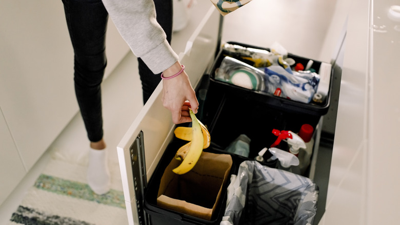 A homeowner placing a banana peel in a compost bin