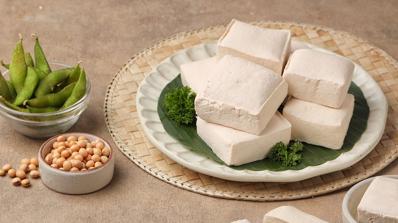 Blocks of tofu on a plate next to soy and edamame beans