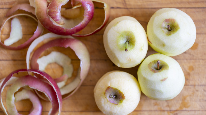 Peeled apples next to apple skins