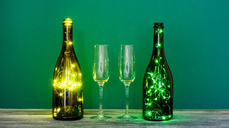 Two wine bottles filled with twinkling light next to two Champagne flutes.