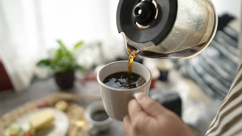 Pouring cup of black coffee from coffee pot