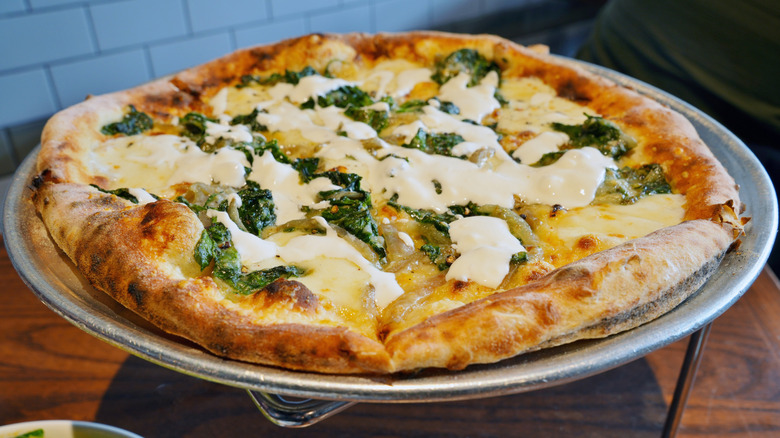 Wood-fired spinach and cheese pizza on metal serving tray
