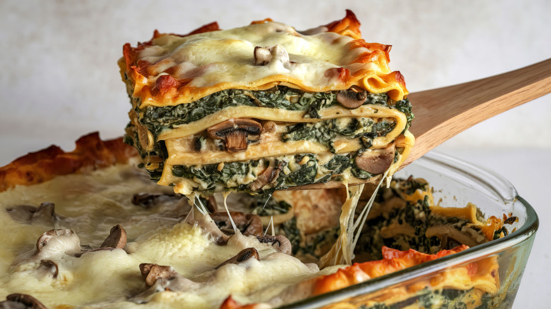 Wooden spatula serving a slice of spinach and mushroom lasagna
