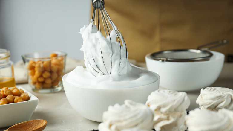 A baker whips aquafaba into a meringue, with cooked swirled meringue cookies in the foreground
