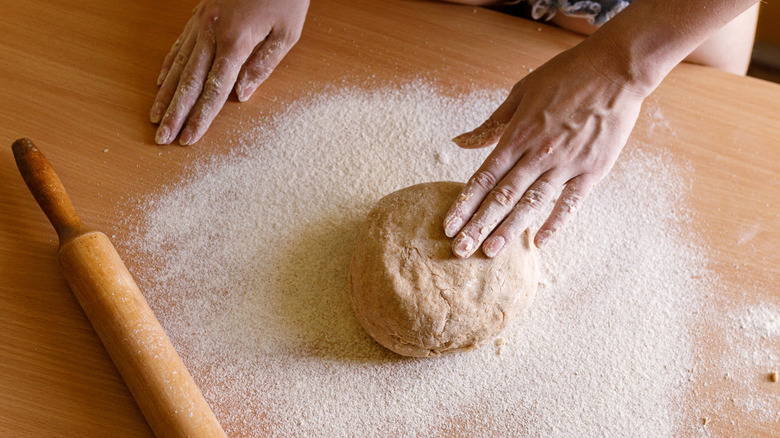 Hands working ball of dough on counter dusted with flour