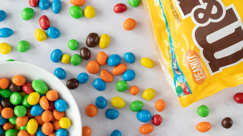 Bowl of M&Ms with open bag of candies scattered around