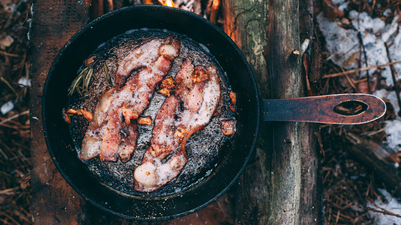 Bacon in pan frying over outdoor fire