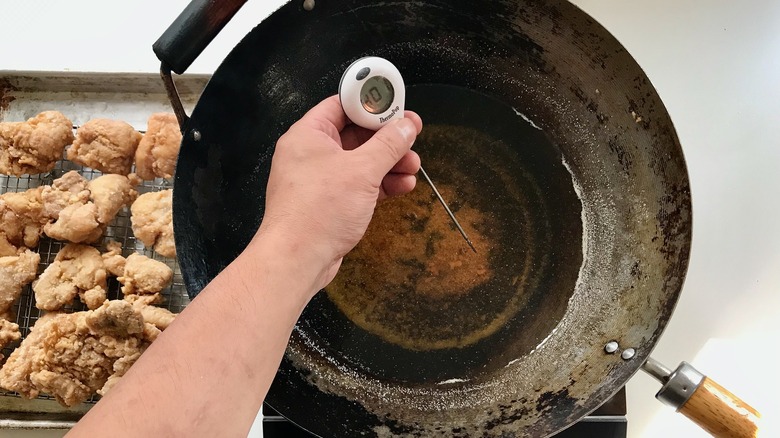 hand holding thermometer in oil