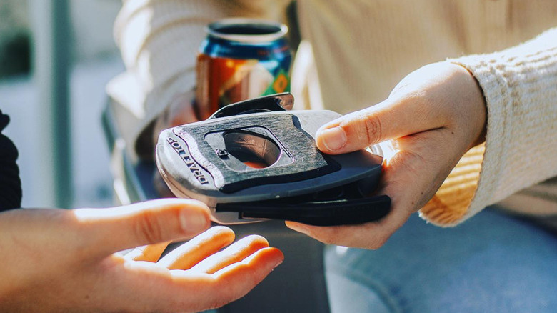One hand giving a can opener to another person