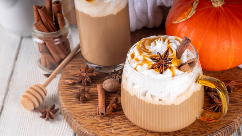 Pumpkin spice latte in a clear cup, next to a small pumpkin and spices.