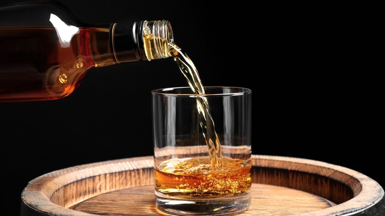 Whiskey being poured into a glass on a barrel 