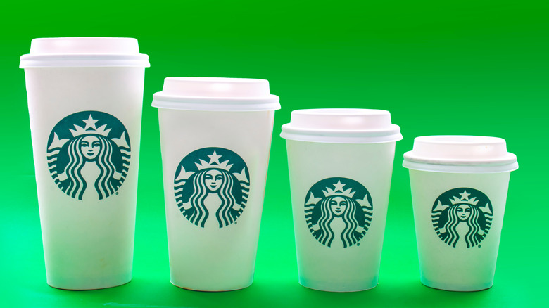 A line of Starbucks cups in different cup sizes against a green background.