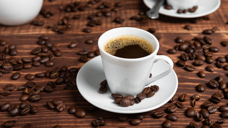 A cup of black coffee surrounded by coffee beans