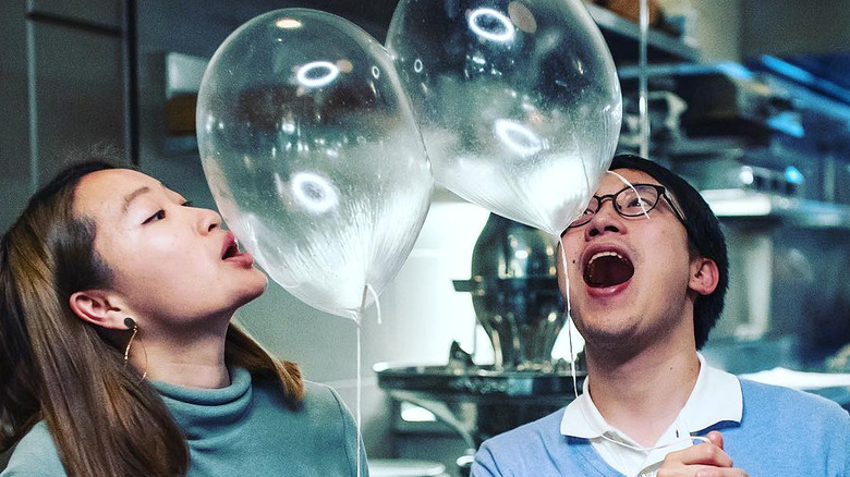 A man and woman opening their mouths to eat clear edible helium balloons