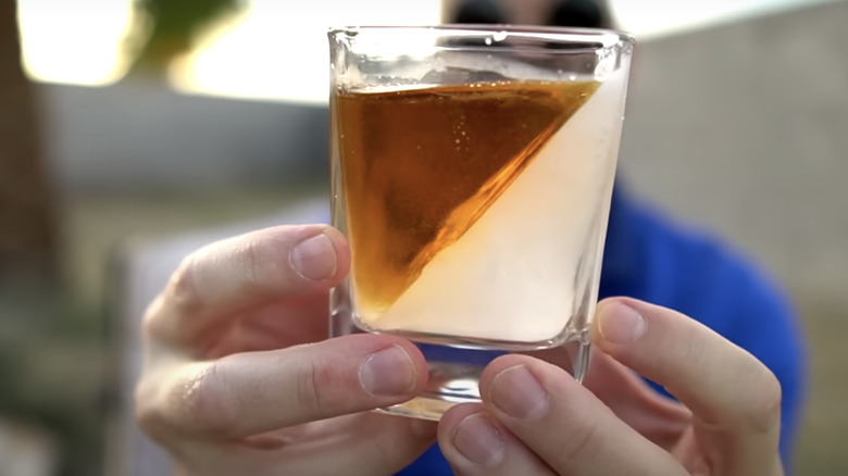 hands holding drink with whiskey wedge cocktail ice