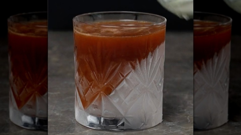 Glass with angled ice and cocktail pouring in