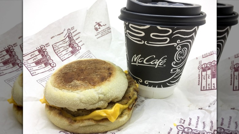 A Sausage McMuffin sits on its unfolded wrapper next to a cup of McCafe coffee.