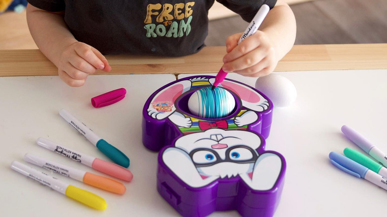 A child uses the Eggmazing Egg Decoration kit to color an egg