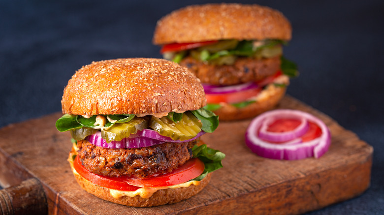Two black bean burgers with all the fixings on a platter sit next to slices of onion and tomato