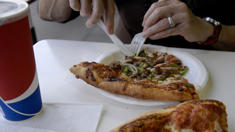 Diner eating Costco pizza topped with peppers.