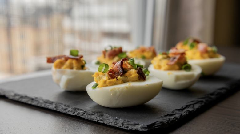 Deviled eggs topped with crumbled bacon and fresh chives sit on a black stone plate
