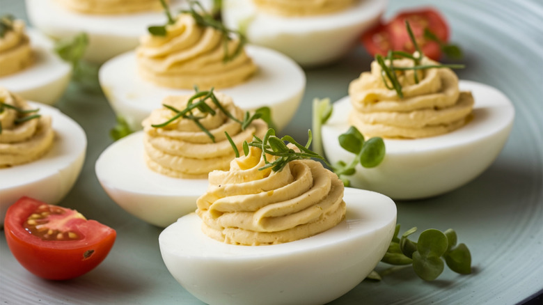 A plate of deviled eggs sits with quartered cherry tomatoes, each egg topped with fresh herbs
