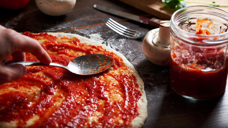 A pizzaiolo spreads pizza sauce onto dough