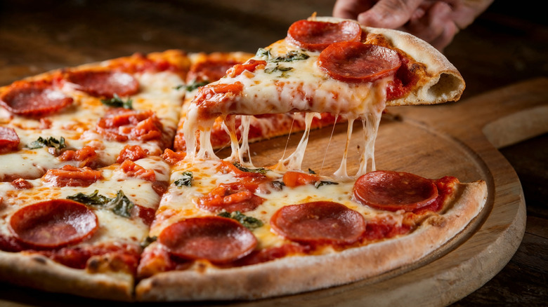 Homemade pizza on a wooden board with one slice being lifted off.