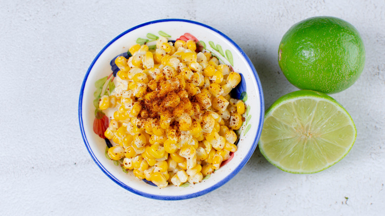 A bowl of esquites or maicitos next to sliced limes.