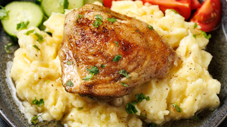 A roasted chicken thigh sits on a bed of mashed potatoes