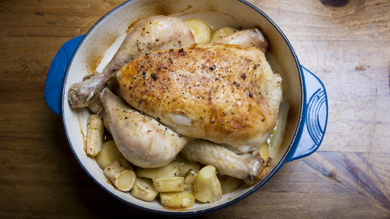 A whole chicken sits in a dutch oven with vegetables