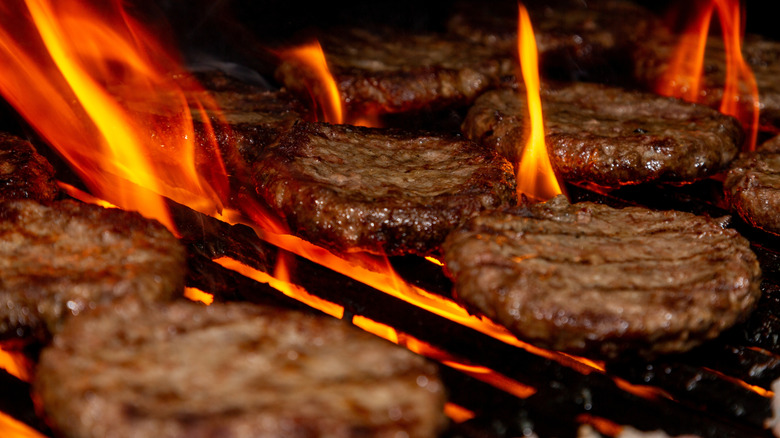 Hamburger patties being grilled over open flames
