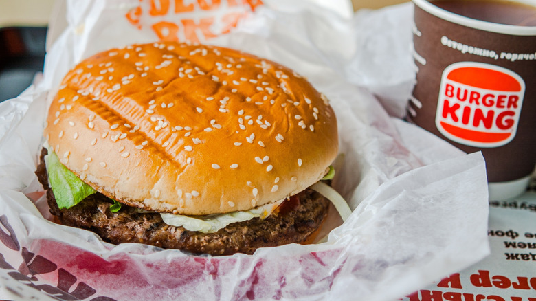 Closeup of an unwrapped Whopper sitting next to a cup of Burger King coffee