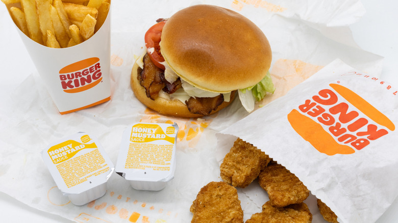 Burger King chicken nuggets, a burger with bacon and Swiss cheese, honey mustard sauce packets, and french fries sit side by side