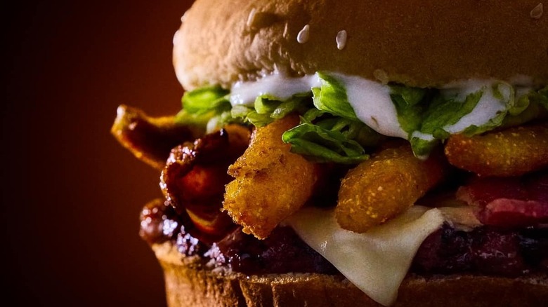 Closeup of a Whopper with ranch dressing, barbecue sauce, bacon, and a breaded, fried topping