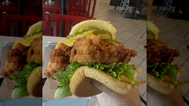 A hand holds a chicken strip sandwich from Chick-fil-A.