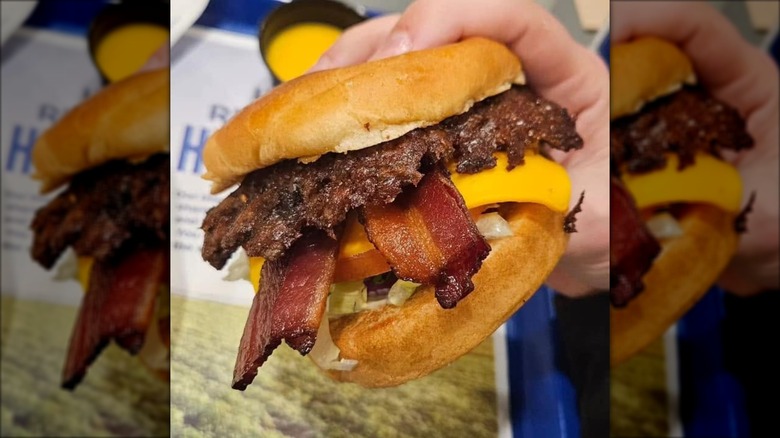 A hand holds up a Culver's ButterBurger with bacon, cheese, lettuce, and tomato on it