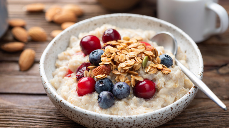 A bowl of oatmeal with berries and granola and a cup of coffee in the background