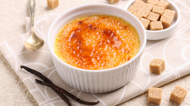 A ramekin of creme brulee surrounded by sugar cubes and vanilla pods