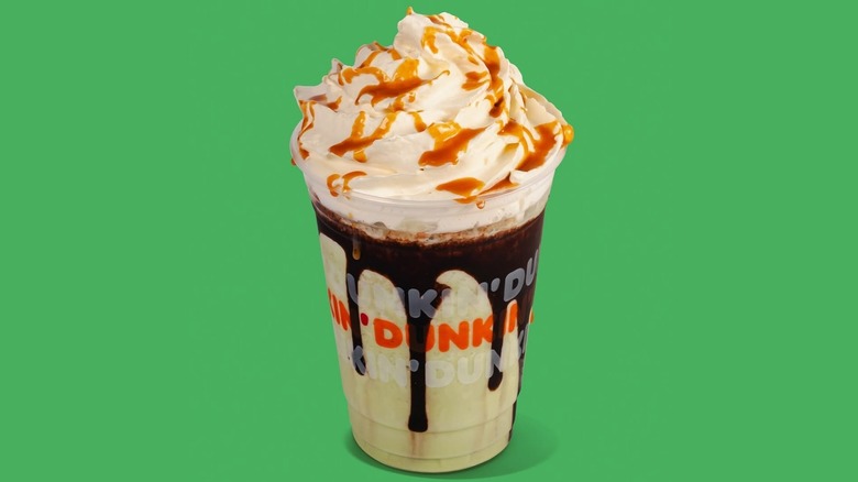 A sweet Dunkin' latte has mocha drizzle around the sides of the cup and caramel sauce on top of the whipped cream.