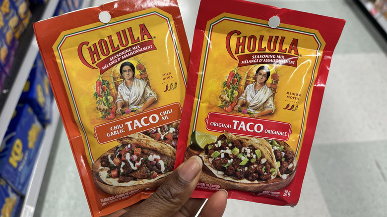 A hand holds two taco seasoning packets at the grocery store