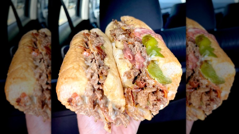 A hand holding two steak bomb sandwiches.