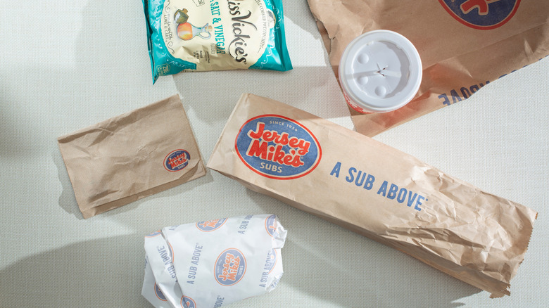 A Jersey Mike's bag with small wrapped sub, bag of chips, and a drink.