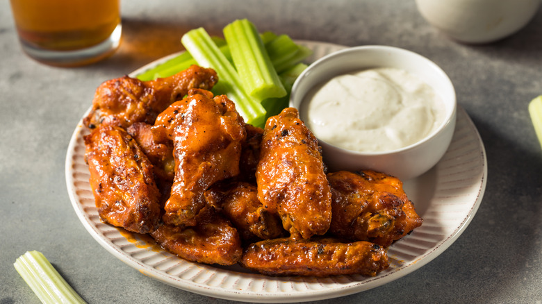 A plate of Buffalo chicken wings with a side of ranch dipping sauce and celery sticks.