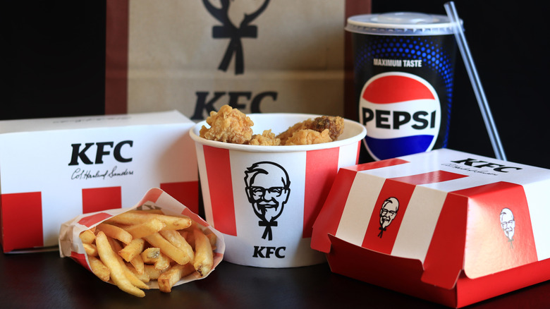 A bucket of KFC fried chicken with fries and boxed sides and a Pepsi.