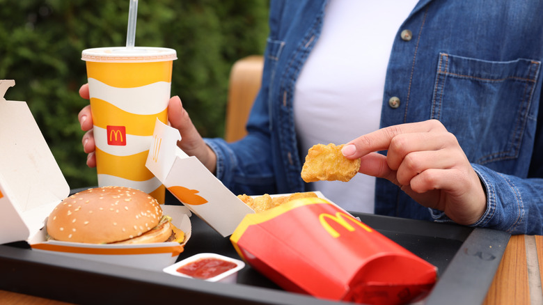 A person holding a McDonald's nugget alongside fries and a burger