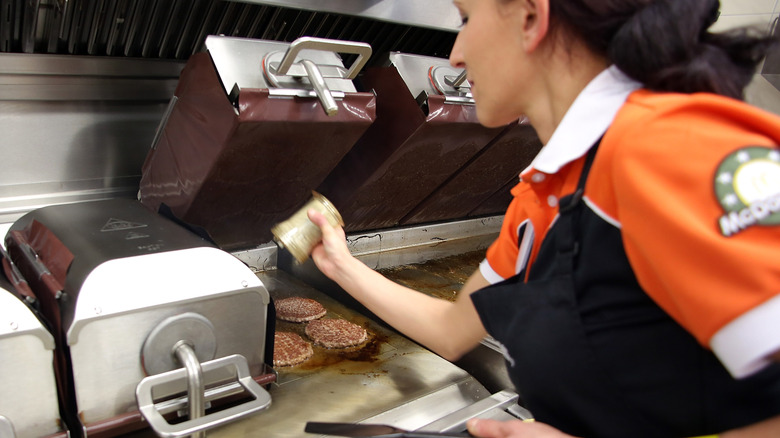 A McDonald's worker seasons burger patties as they cook